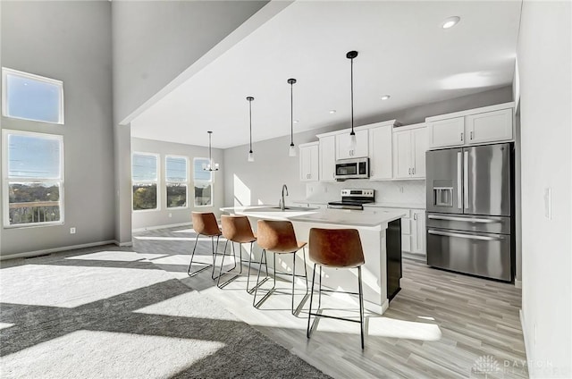 kitchen featuring appliances with stainless steel finishes, a breakfast bar area, a center island with sink, white cabinets, and light countertops