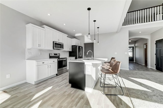 kitchen with appliances with stainless steel finishes, a sink, arched walkways, light countertops, and a center island with sink