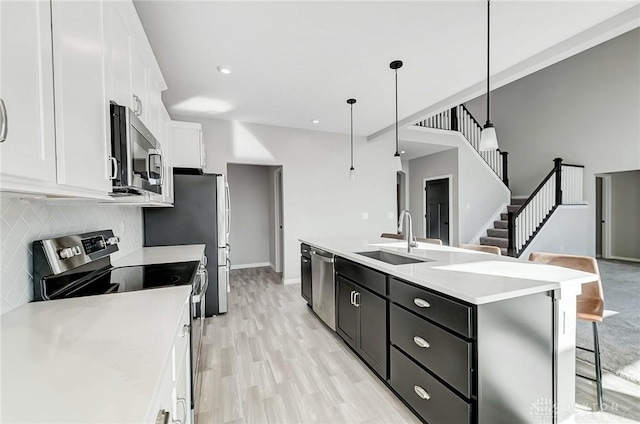 kitchen featuring stainless steel appliances, a sink, white cabinets, light countertops, and a center island with sink