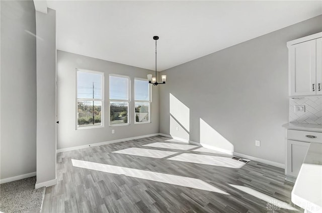 unfurnished dining area featuring a chandelier, baseboards, and light wood-style floors