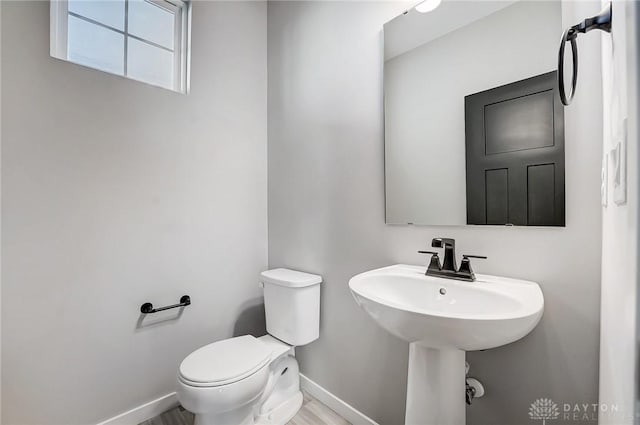 half bathroom featuring baseboards, toilet, and a sink