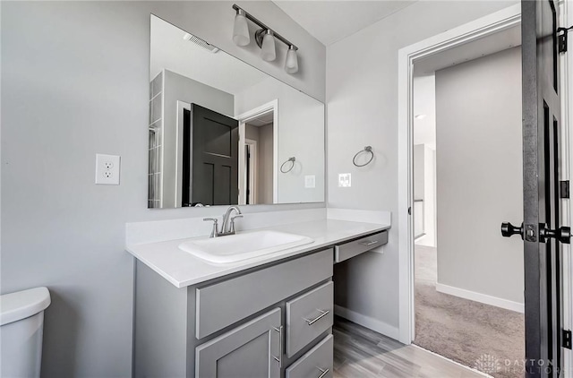 bathroom with toilet, vanity, baseboards, and wood finished floors
