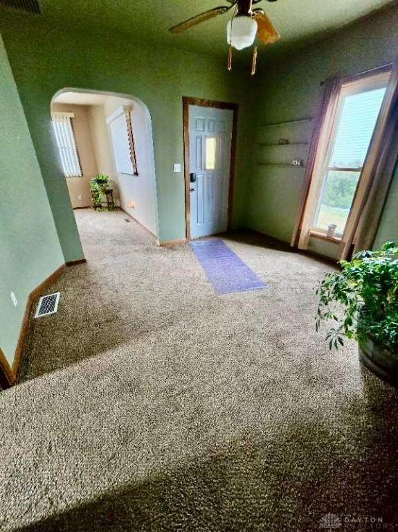 foyer featuring a ceiling fan, carpet, arched walkways, and visible vents