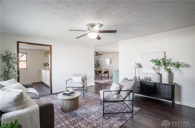 living room featuring dark wood-type flooring, ceiling fan, and a textured ceiling