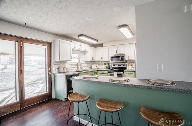 kitchen with dark wood-type flooring, sink, kitchen peninsula, stainless steel appliances, and white cabinets