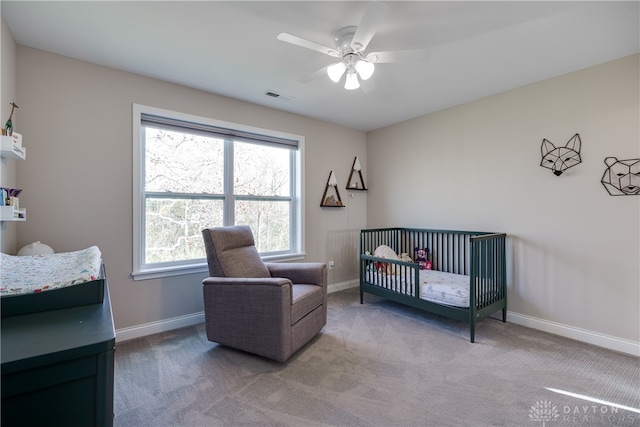 carpeted bedroom featuring ceiling fan and a nursery area