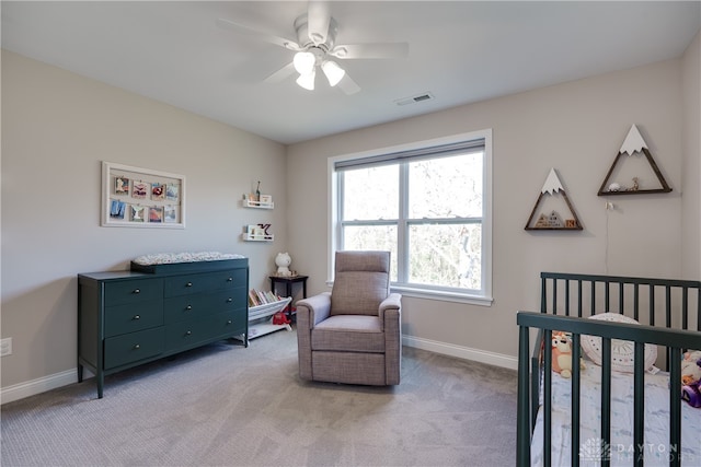 bedroom featuring a crib, light colored carpet, and ceiling fan