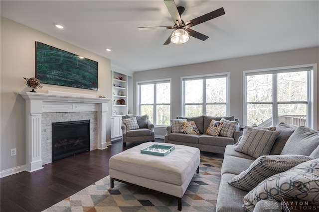 living room with a brick fireplace, dark hardwood / wood-style floors, built in shelves, and ceiling fan