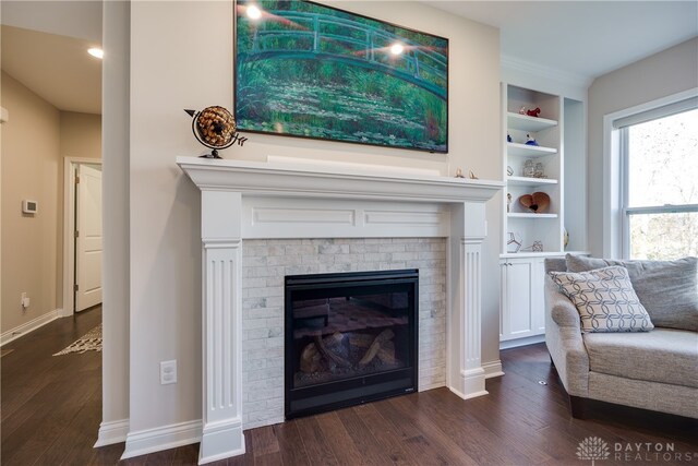 living room with a brick fireplace, built in shelves, and dark hardwood / wood-style flooring