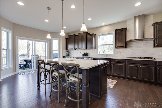 kitchen with a kitchen breakfast bar, dark hardwood / wood-style floors, a kitchen island, wall chimney range hood, and pendant lighting