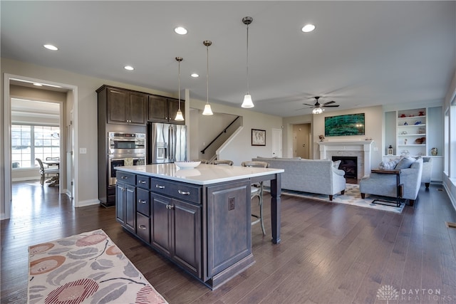 kitchen with stainless steel appliances, dark brown cabinetry, pendant lighting, dark wood-type flooring, and a kitchen island with sink