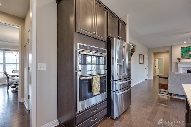 kitchen featuring a fireplace, dark hardwood / wood-style flooring, dark brown cabinets, and appliances with stainless steel finishes