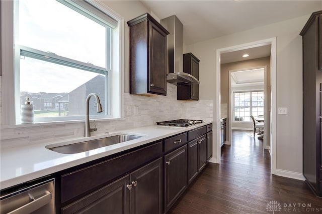 kitchen featuring wall chimney range hood, appliances with stainless steel finishes, backsplash, sink, and dark wood-type flooring