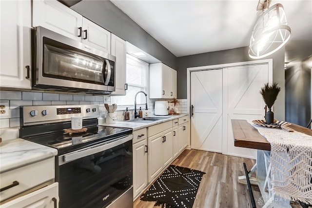 kitchen featuring stainless steel appliances, sink, hanging light fixtures, white cabinets, and light wood-type flooring