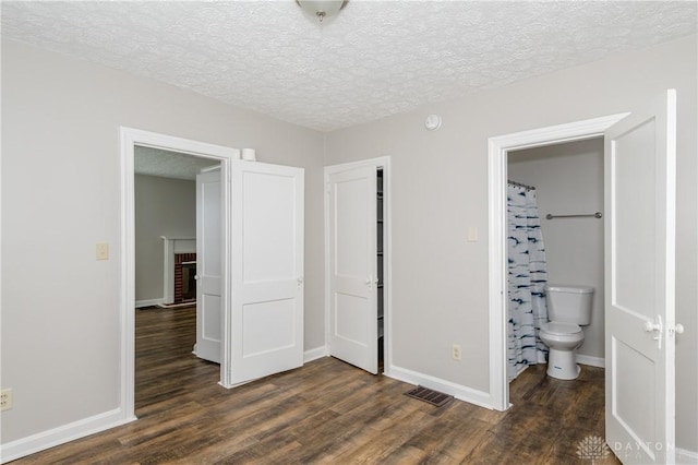 unfurnished bedroom featuring dark wood-type flooring, connected bathroom, a textured ceiling, and a fireplace