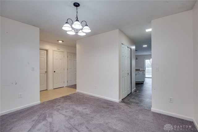 empty room featuring a notable chandelier, carpet floors, and baseboards