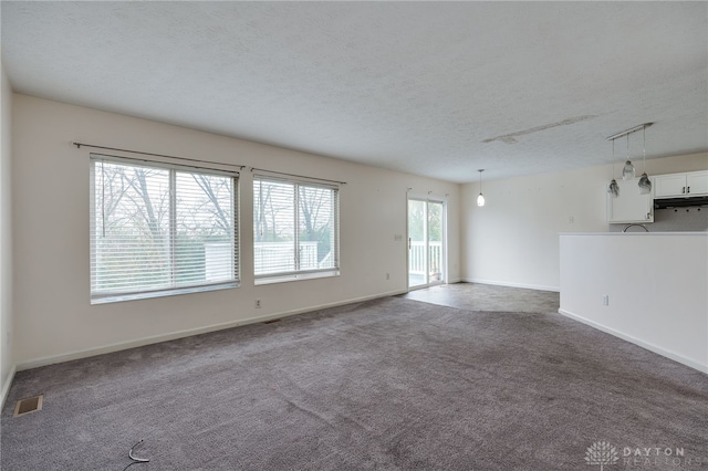 unfurnished living room featuring a textured ceiling, carpet, visible vents, and baseboards