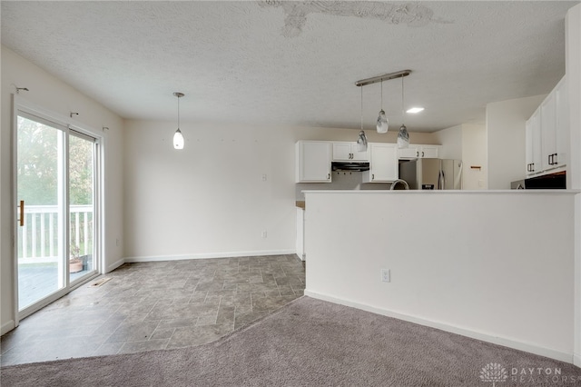 kitchen featuring under cabinet range hood, white cabinetry, baseboards, stainless steel fridge, and decorative light fixtures