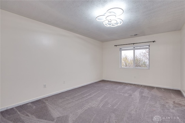 spare room featuring carpet, visible vents, baseboards, and a textured ceiling