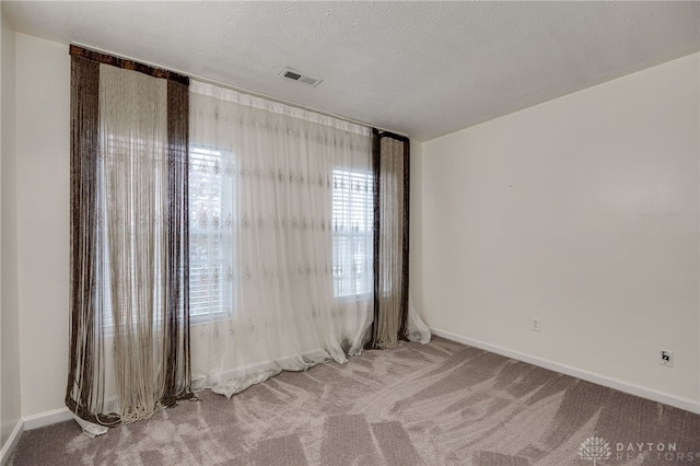 spare room featuring carpet floors, visible vents, a textured ceiling, and baseboards