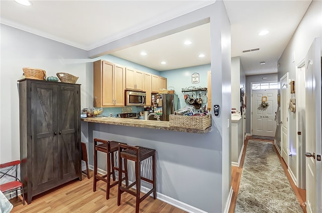 kitchen with stainless steel appliances, light brown cabinets, a breakfast bar, light hardwood / wood-style floors, and kitchen peninsula