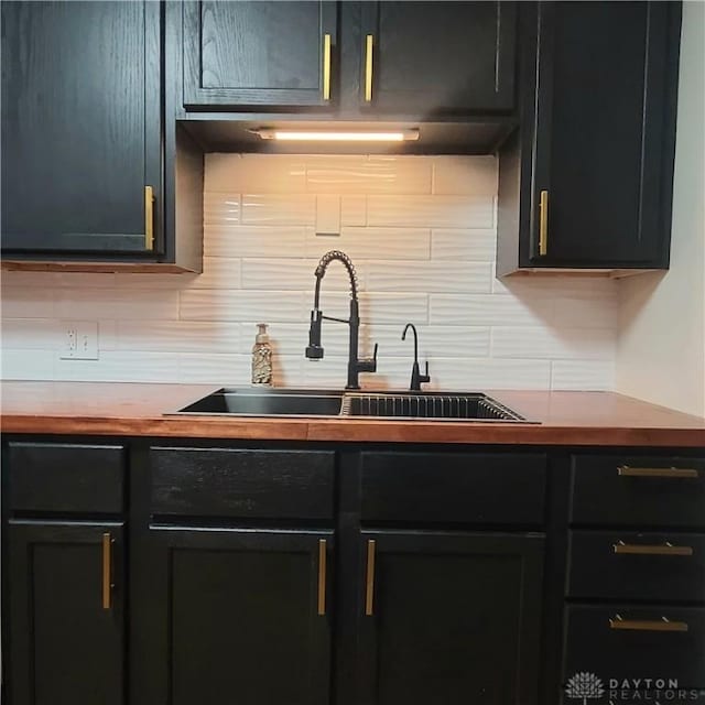 kitchen featuring dark cabinets, wood counters, decorative backsplash, and a sink