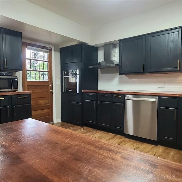 kitchen featuring oven, stainless steel dishwasher, light wood-type flooring, wall chimney exhaust hood, and tasteful backsplash