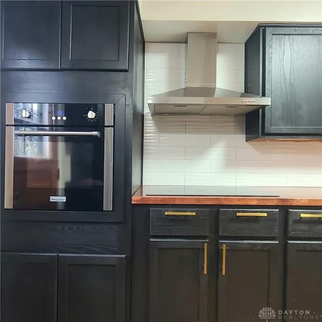 kitchen with black electric stovetop, oven, wooden counters, decorative backsplash, and wall chimney exhaust hood