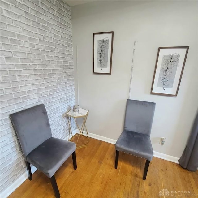 living area with brick wall, baseboards, and wood finished floors