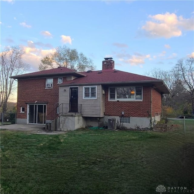 view of front of house with brick siding, a patio, a chimney, cooling unit, and a front yard