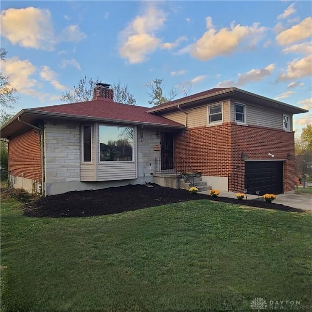 split level home featuring driveway, a garage, stone siding, a chimney, and a front yard