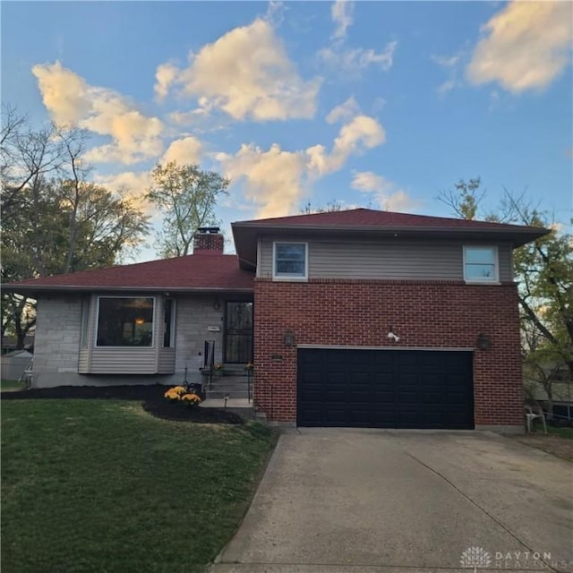 split level home with a garage, brick siding, driveway, a chimney, and a front yard