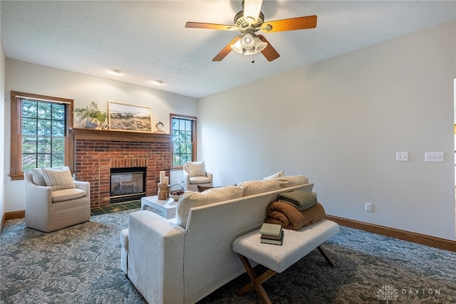 living room featuring a textured ceiling, dark colored carpet, ceiling fan, and a brick fireplace