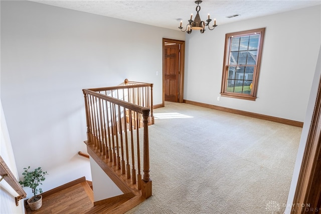 staircase featuring carpet floors, a notable chandelier, and a textured ceiling