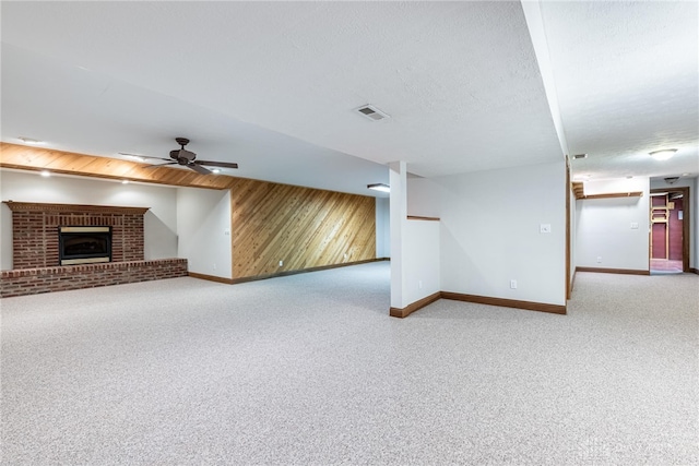 unfurnished living room with wood walls, ceiling fan, a textured ceiling, carpet flooring, and a fireplace