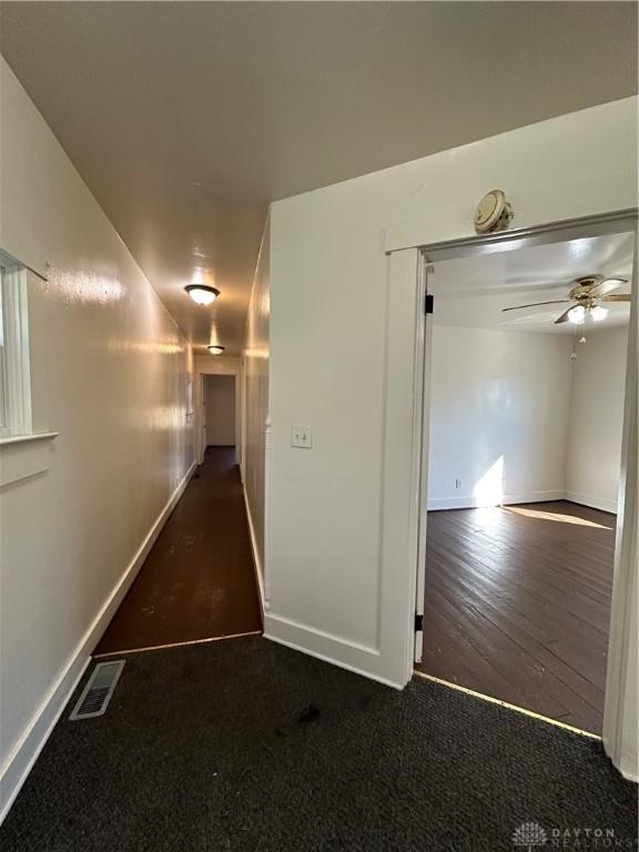 hallway featuring carpet, wood finished floors, visible vents, and baseboards