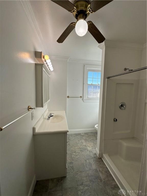 bathroom with a shower, toilet, ornamental molding, vanity, and baseboards