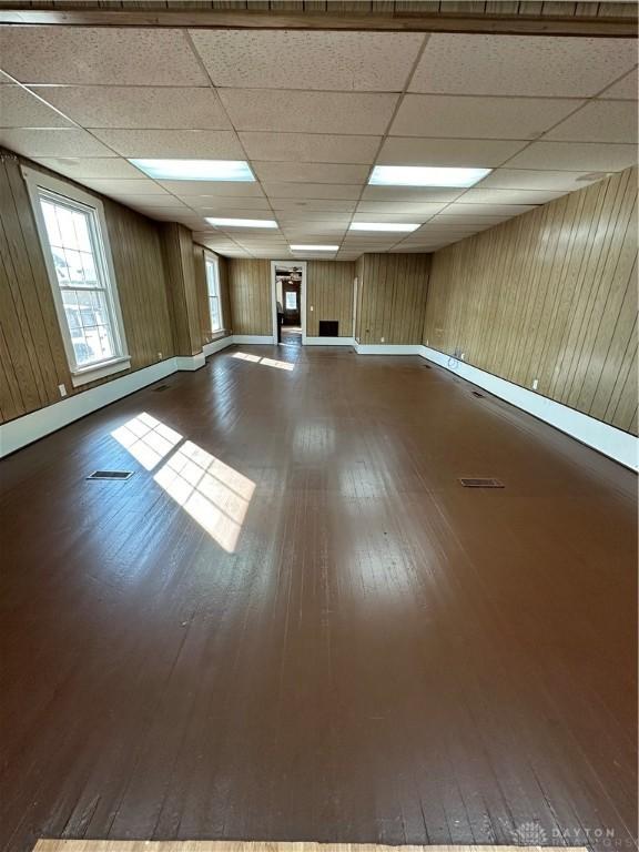 below grade area featuring wood walls, dark wood-style flooring, a paneled ceiling, and baseboards