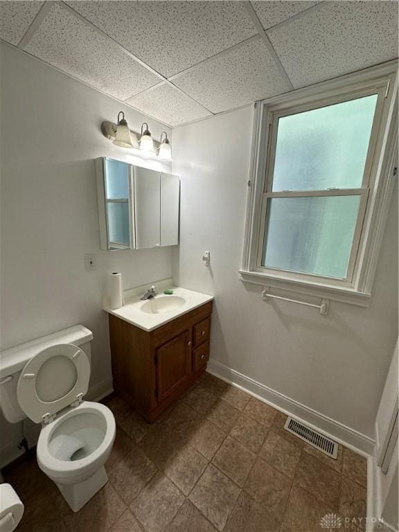 bathroom featuring toilet, baseboards, visible vents, and a paneled ceiling