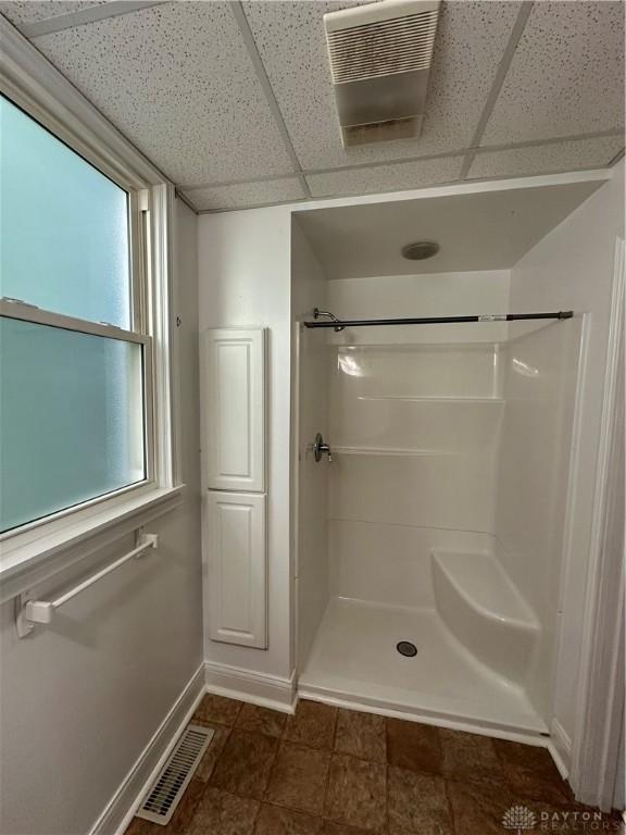 bathroom with a shower, a drop ceiling, visible vents, and baseboards