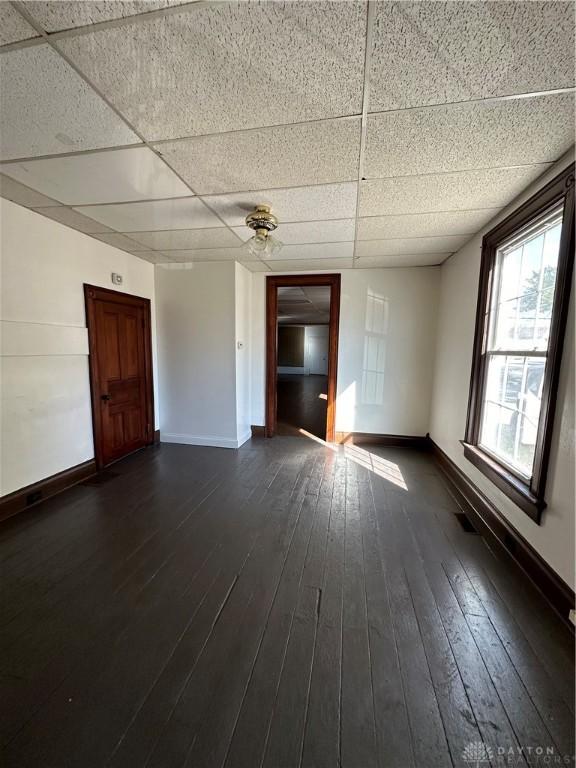 spare room featuring dark wood-type flooring, a drop ceiling, and baseboards