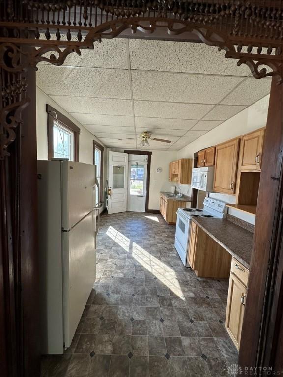 kitchen featuring white appliances, brown cabinetry, and a drop ceiling