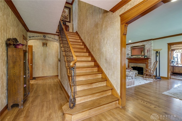 stairway with hardwood / wood-style floors, a large fireplace, a textured ceiling, and crown molding