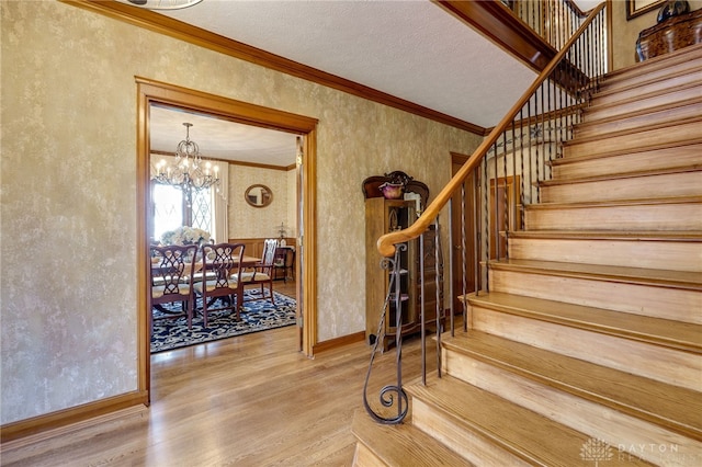 stairway featuring a textured ceiling, an inviting chandelier, hardwood / wood-style flooring, and crown molding