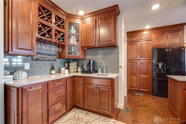 kitchen with hardwood / wood-style floors, black fridge with ice dispenser, sink, and backsplash