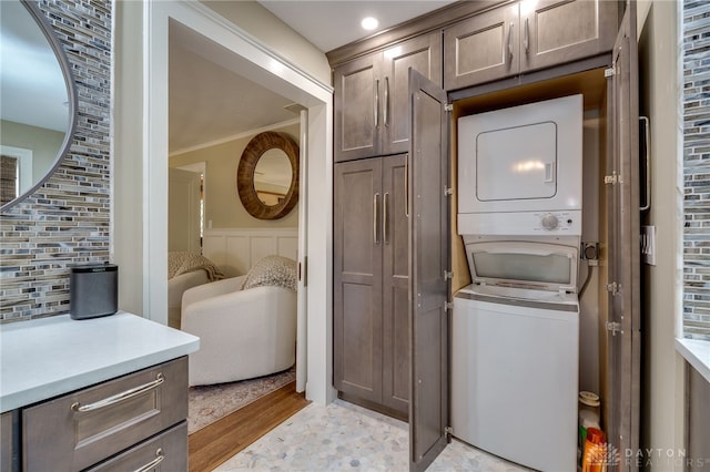 laundry room featuring stacked washer / drying machine, ornamental molding, and light hardwood / wood-style flooring