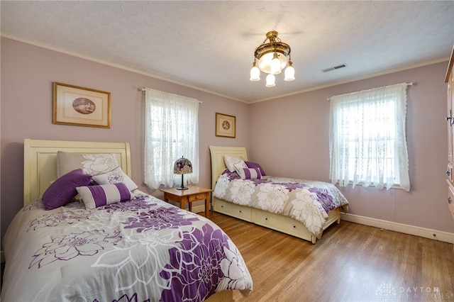 bedroom featuring ornamental molding, an inviting chandelier, a textured ceiling, and light hardwood / wood-style floors