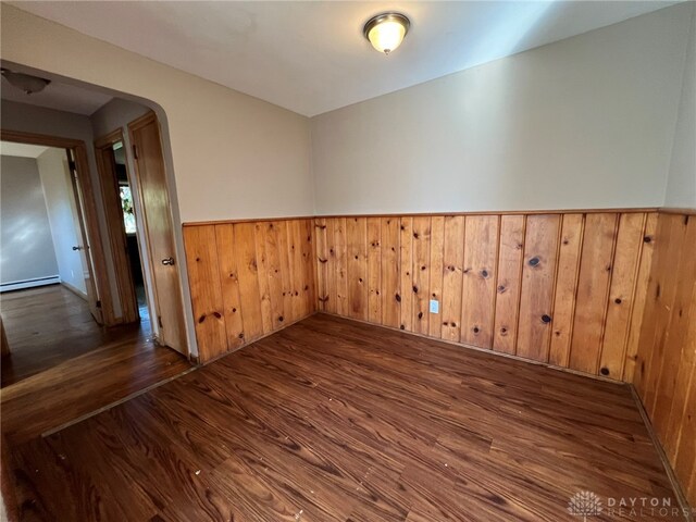 spare room featuring dark wood-type flooring, wooden walls, and a baseboard heating unit