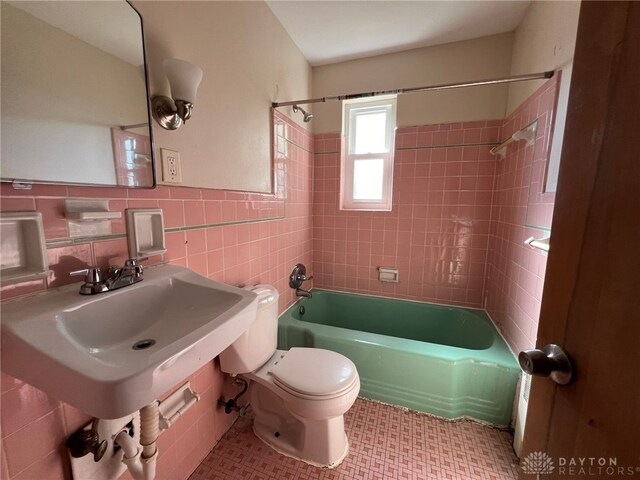 bathroom featuring tiled shower / bath, toilet, and tile walls