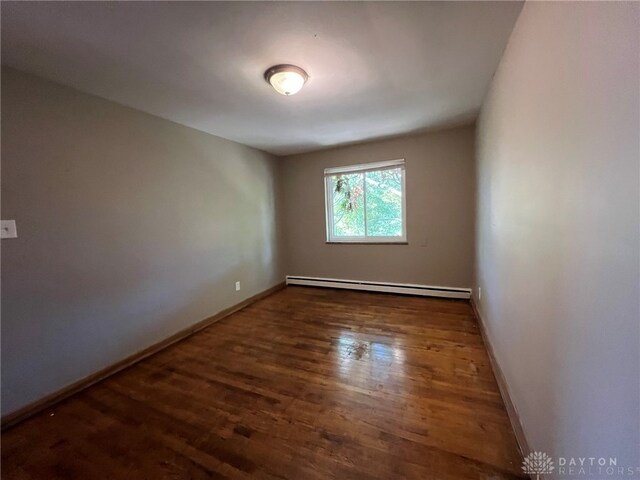 unfurnished room featuring dark hardwood / wood-style flooring and a baseboard heating unit